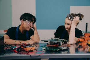 Two young engineers at a workbench, collaborating on electronics with circuit boards.